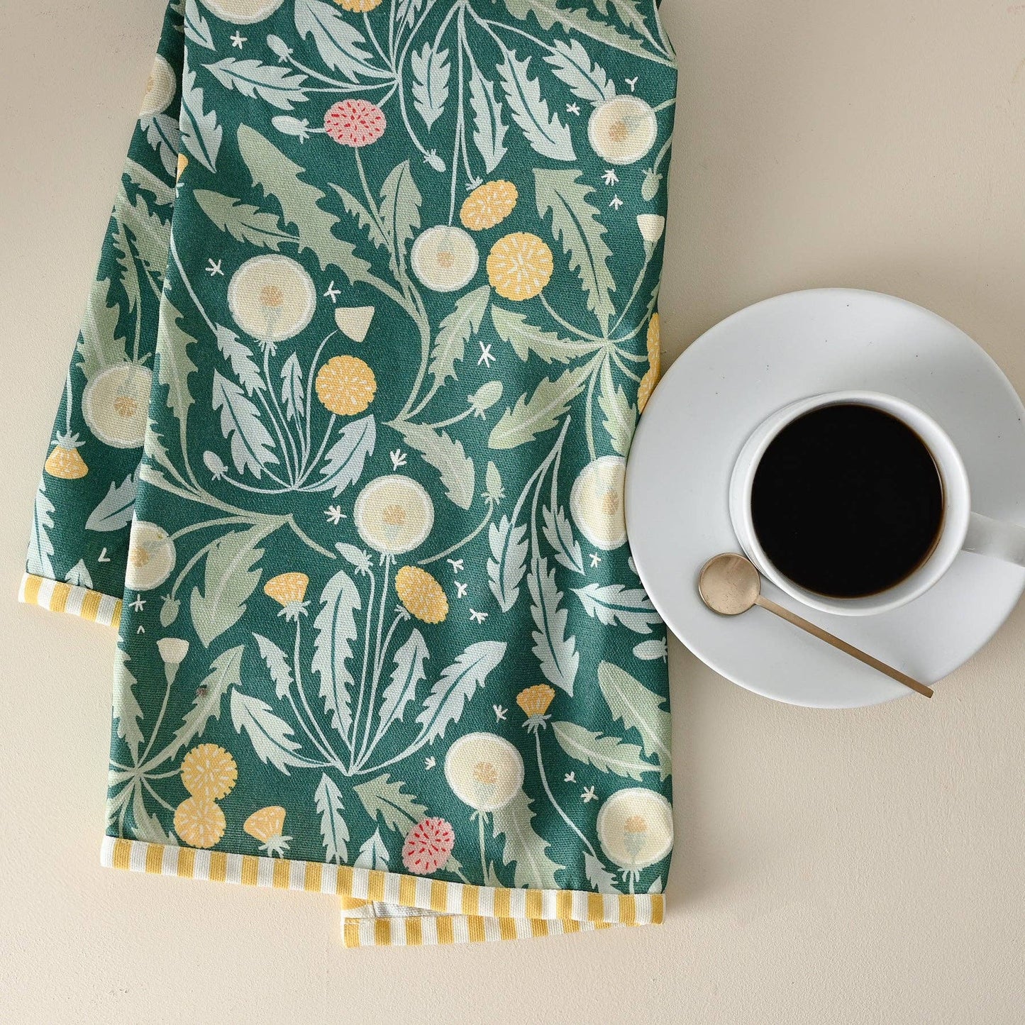 Tea towel with floral pattern next to a cup of coffee on a beige surface