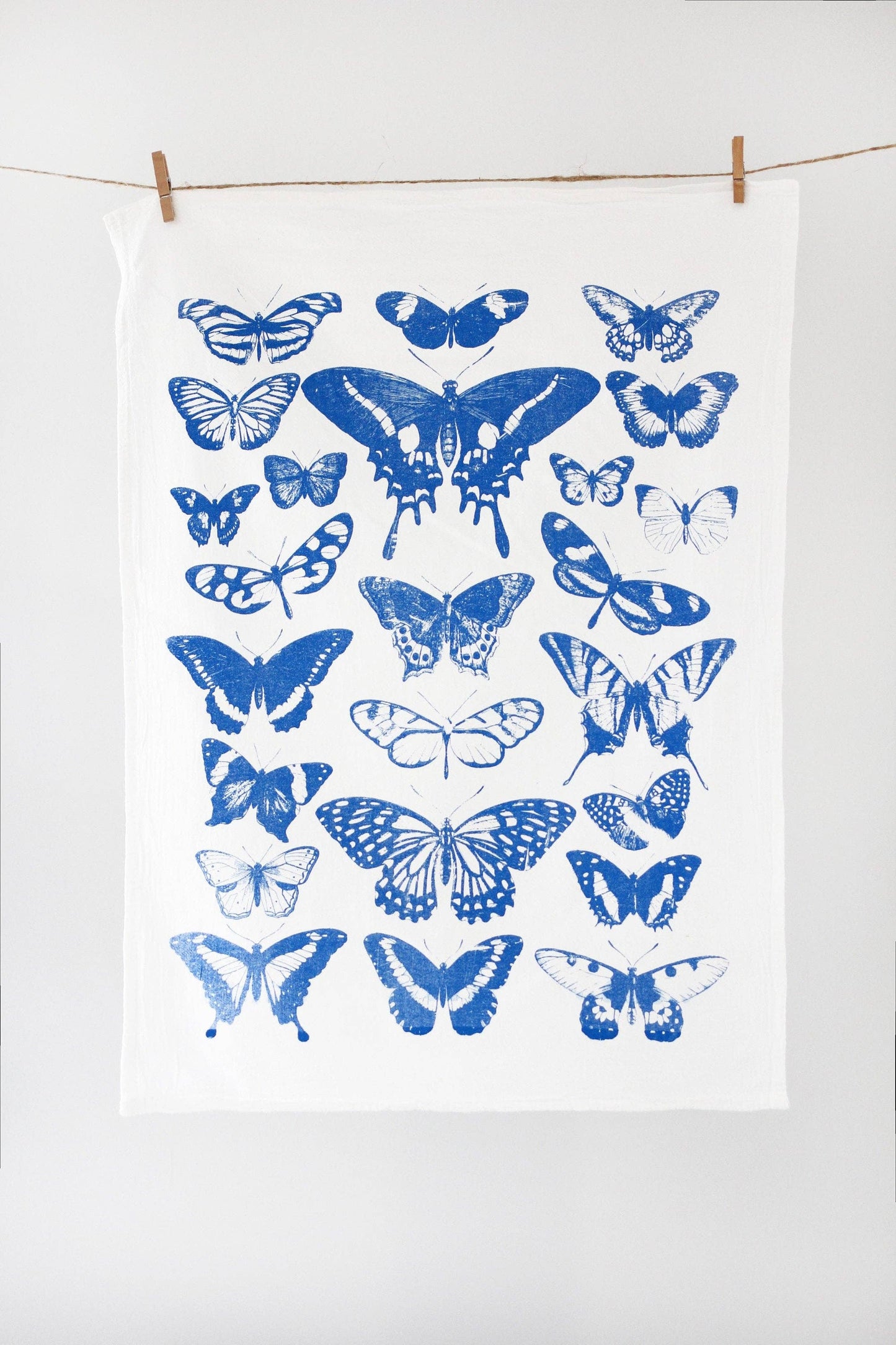 White towel with blue butterfly patterns hanging on a line against a white background
