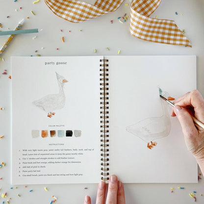 A hand is painting a goose illustration in an open spiral notebook. The left page shows a finished goose drawing, color palette swatches, and step-by-step instructions.