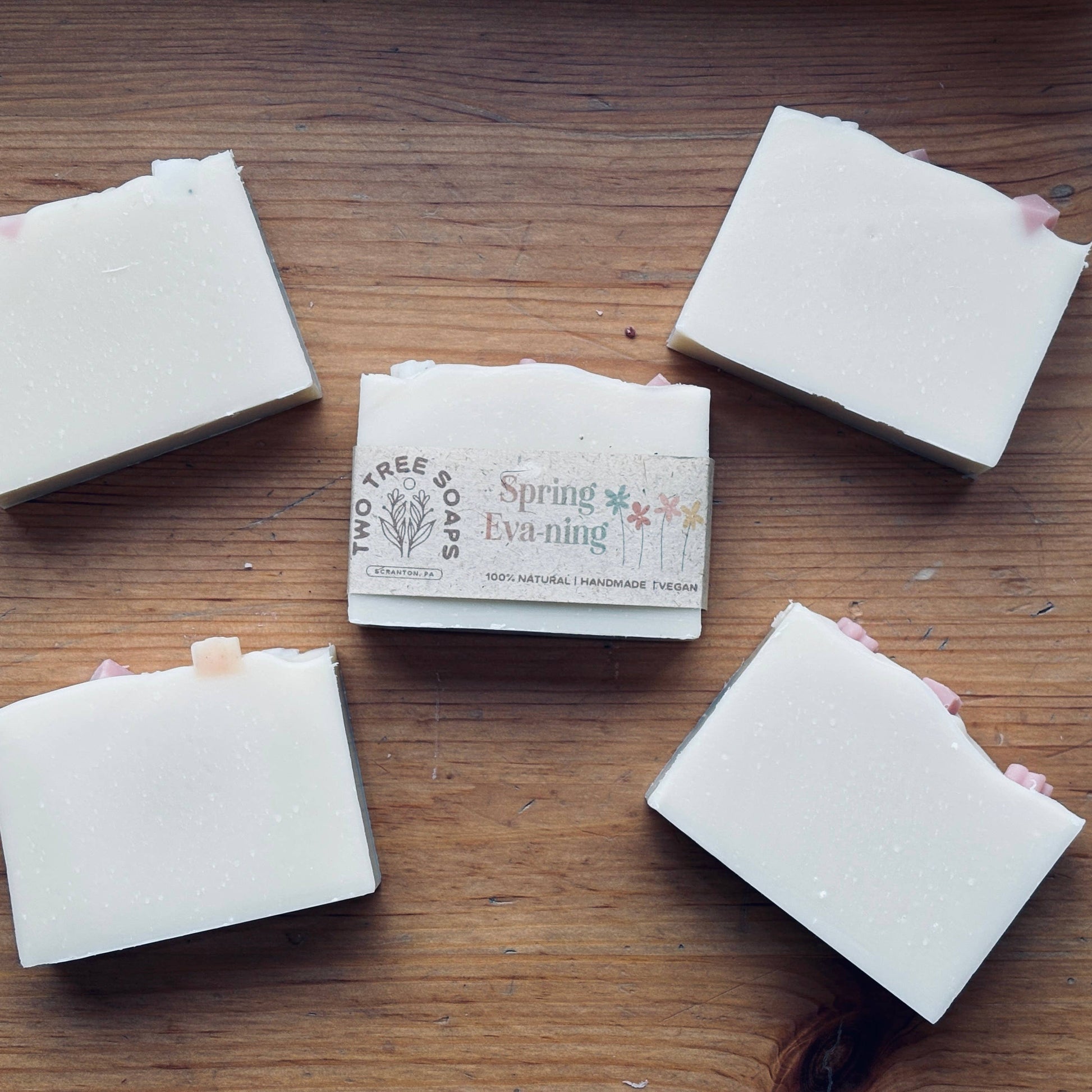 Five square bars of soap on a wooden surface with one bar featuring a 'Spring Evening' label.