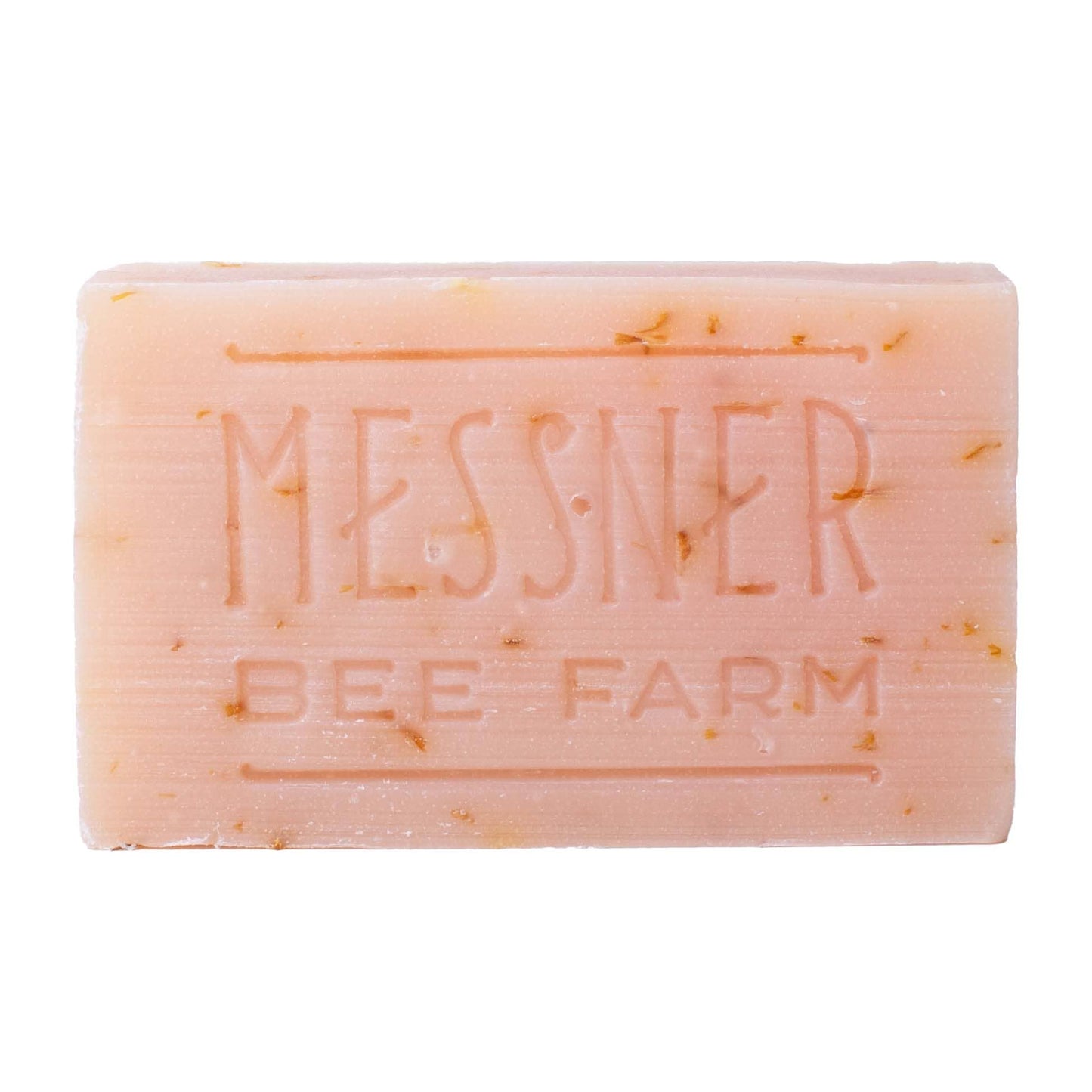 A rectangular bar of Messner Bee Farm soap in a pale peach-pink color, featuring small golden-yellow botanical inclusions and embossed branding on a plain white background.