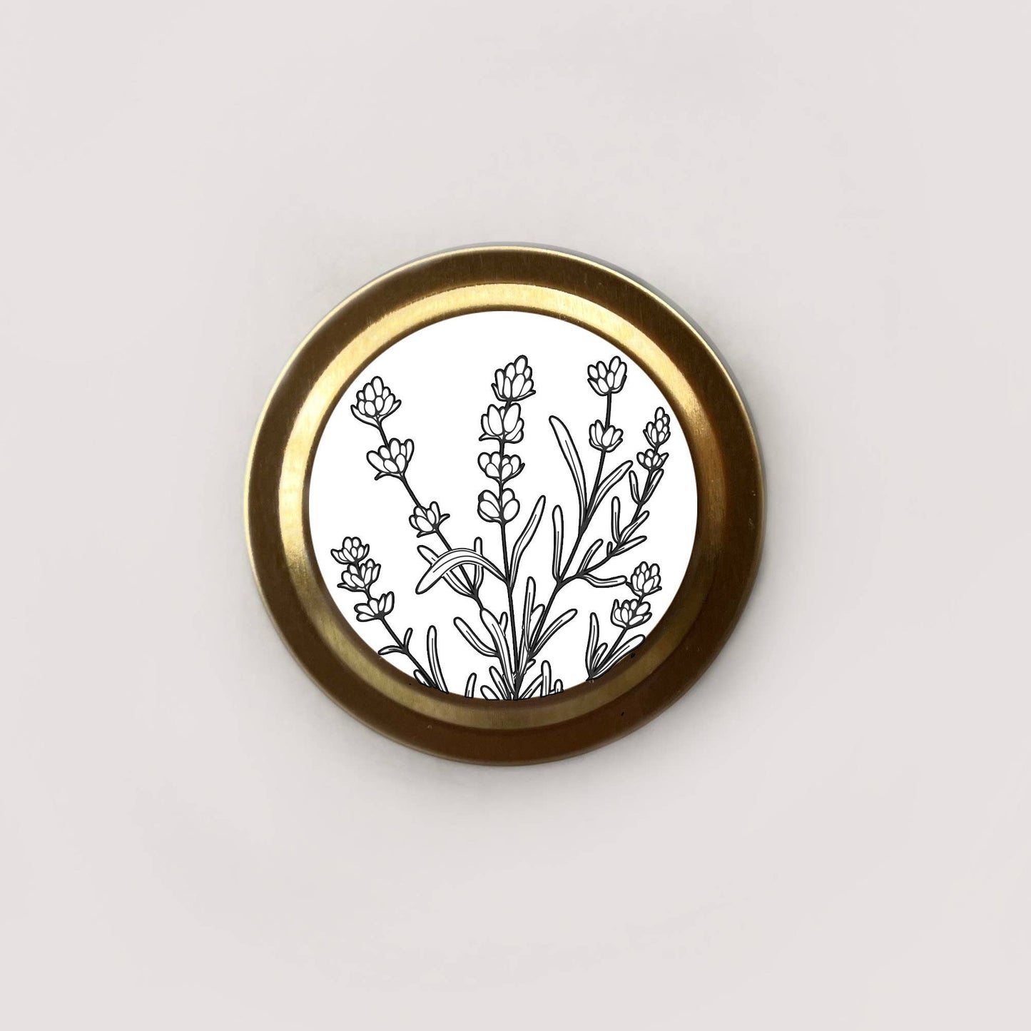 Round brass object with black floral design on a white background
