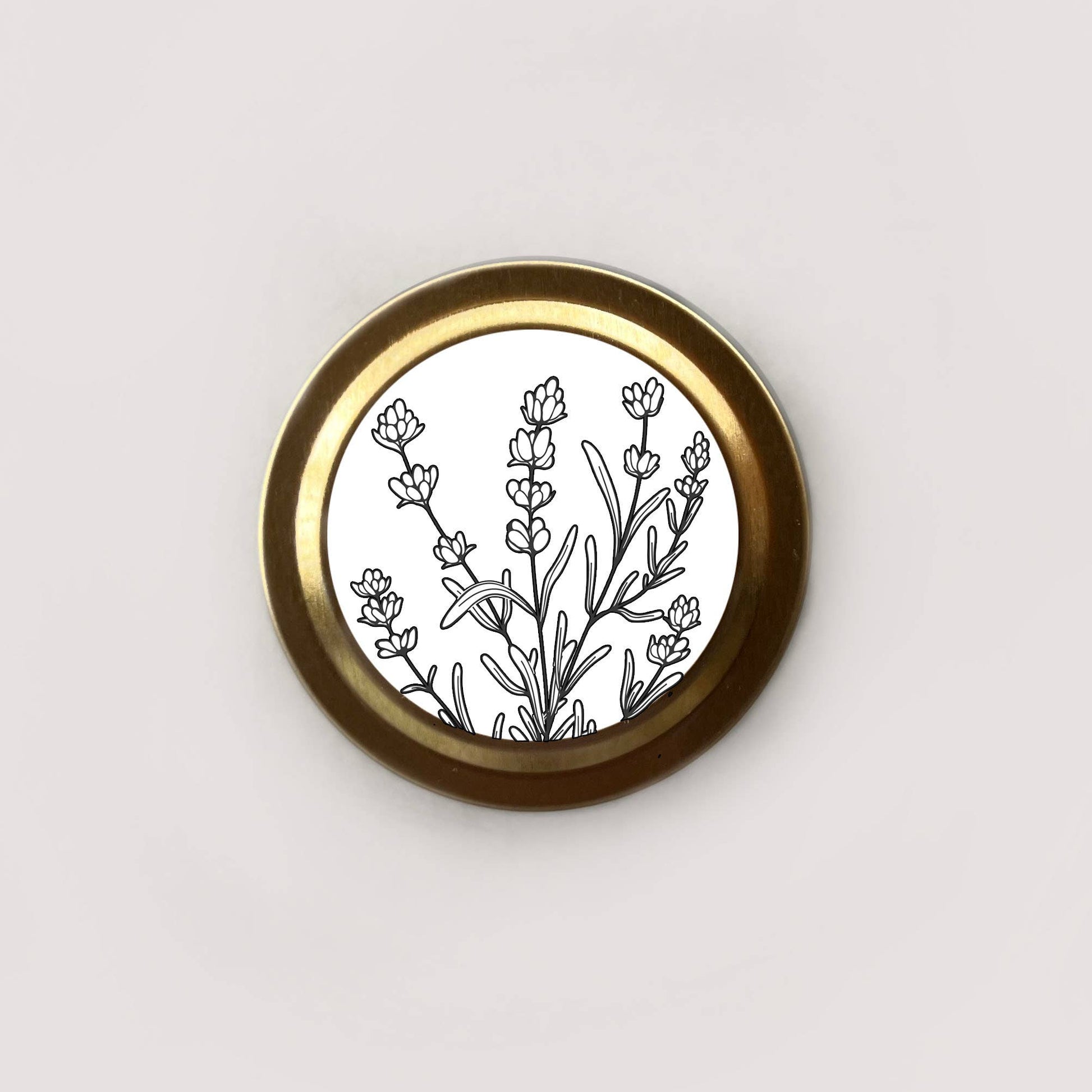Round brass object with black floral design on a white background