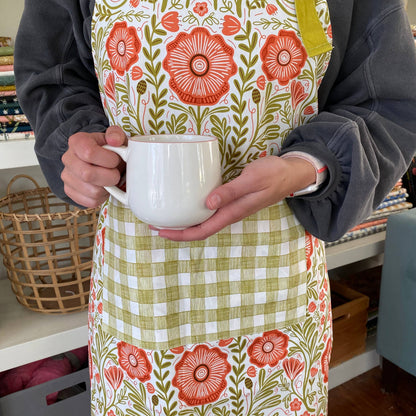 Person wearing a floral apron holding a white mug indoors.