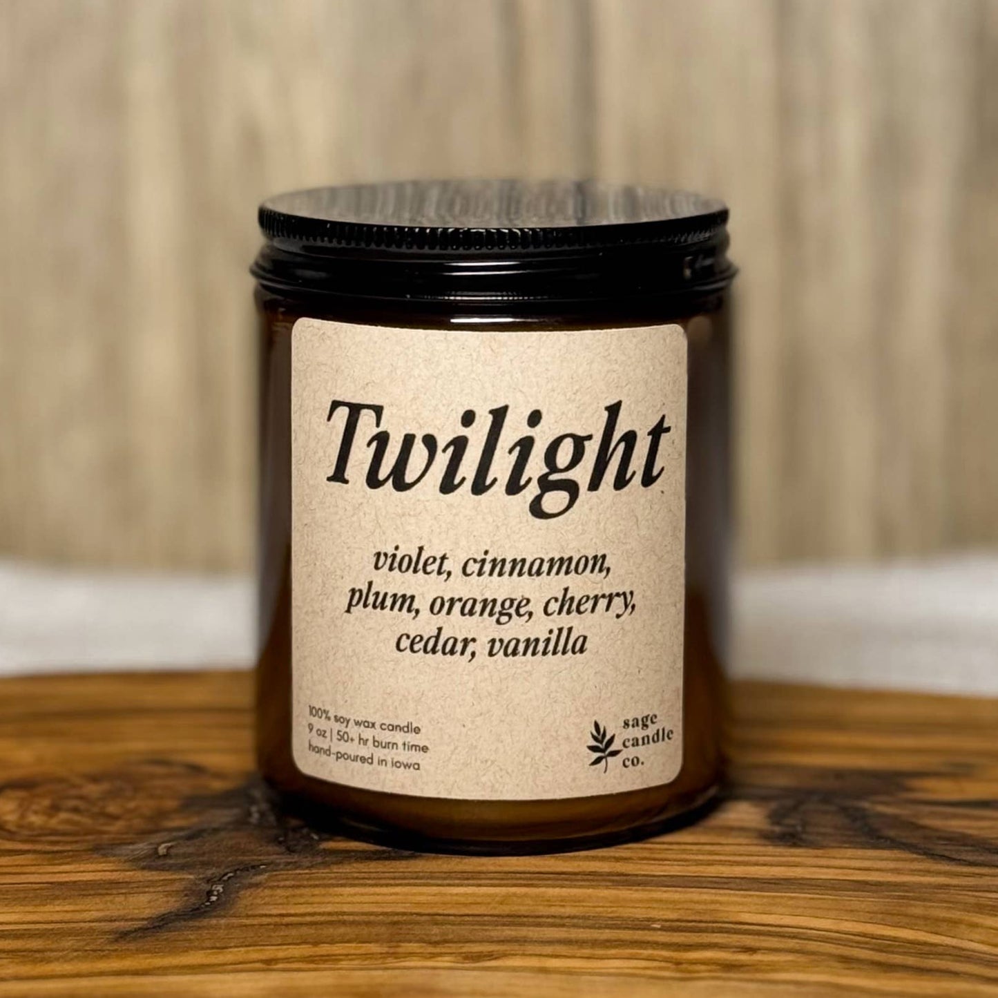 A candle jar labeled 'Twilight' with a black lid and cream label, placed on a rustic wooden board against a light wood background.