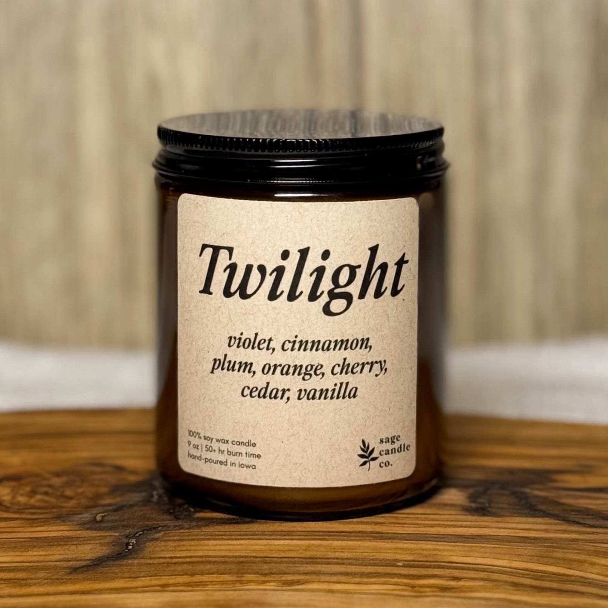 A candle jar labeled 'Twilight' with a black lid and cream label, placed on a rustic wooden board against a light wood background.