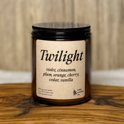 A candle jar labeled 'Twilight' with a black lid and cream label, placed on a rustic wooden board against a light wood background.