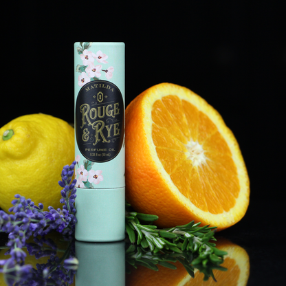 Perfume oil bottle with a lemon, orange, and lavender on a reflective surface