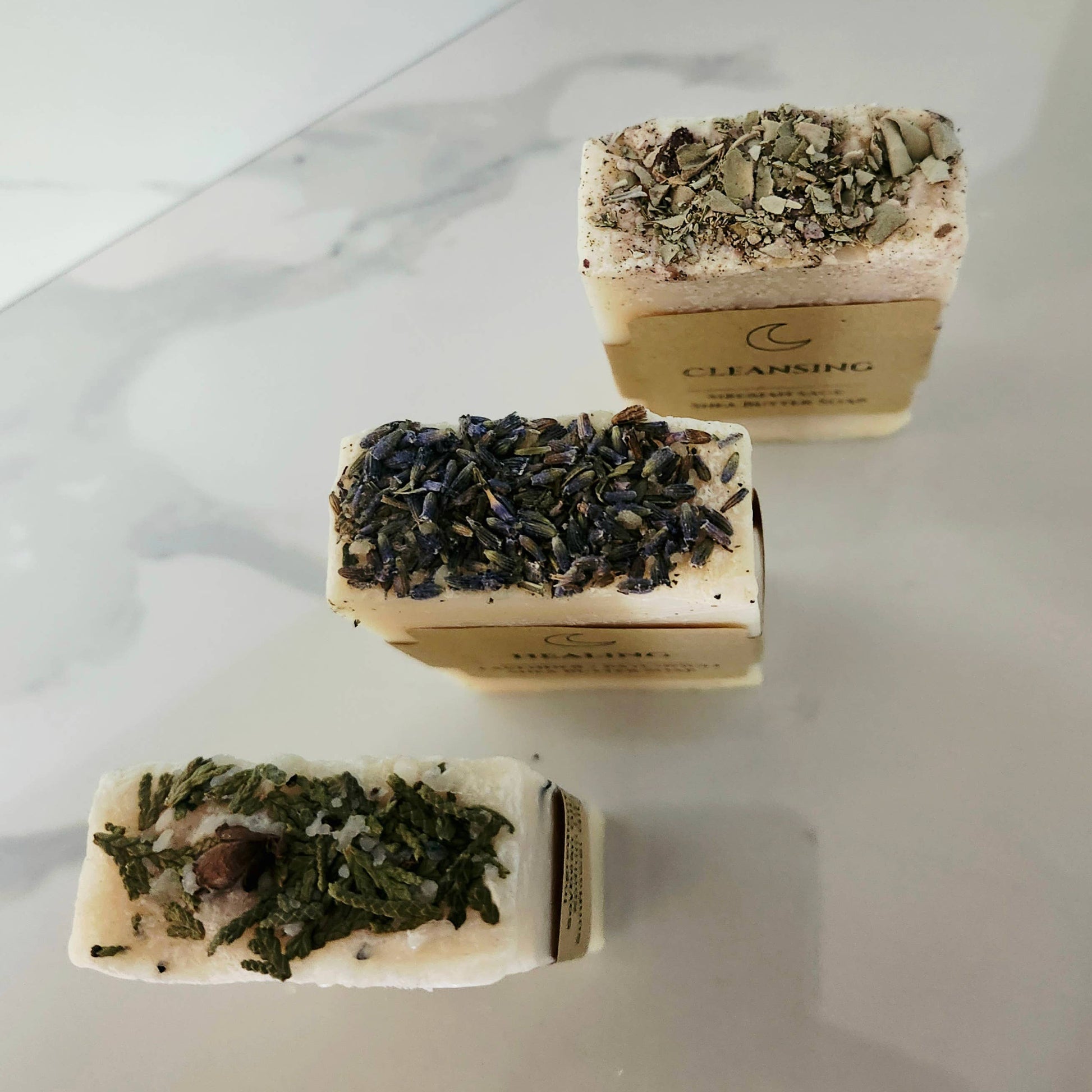 Three rectangular soap bars with green herb mixture on a marble surface
