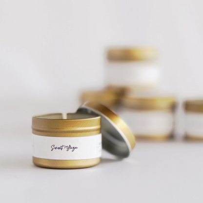 Candle in a gold tin with a white label on a light gray background