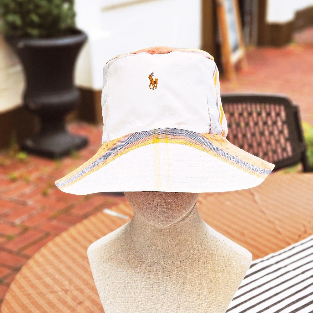 Plaid Bucket Hat using upcyled Ralph Lauren shirt that is white with a summer plaid of blues, yellows, greens, and reds modeled on a mannequin head on a outdoor cafe table. 