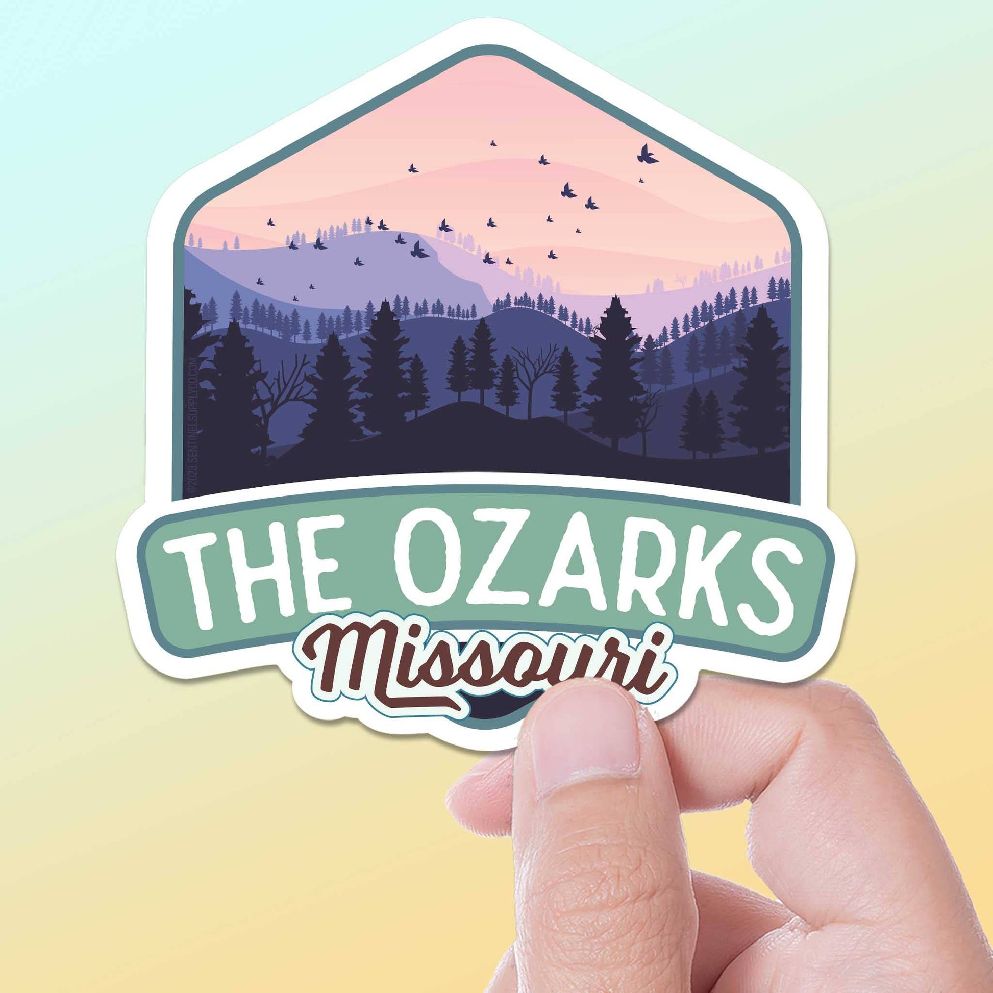 Sticker with 'The Ozarks Missouri' design held by a hand on a gradient background