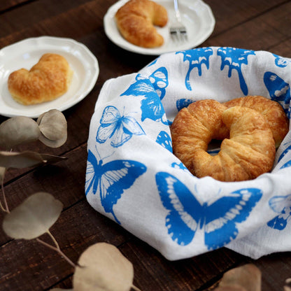 Croissants in a butterfly-patterned cloth on a wooden table with heart-shaped pastries in the background.