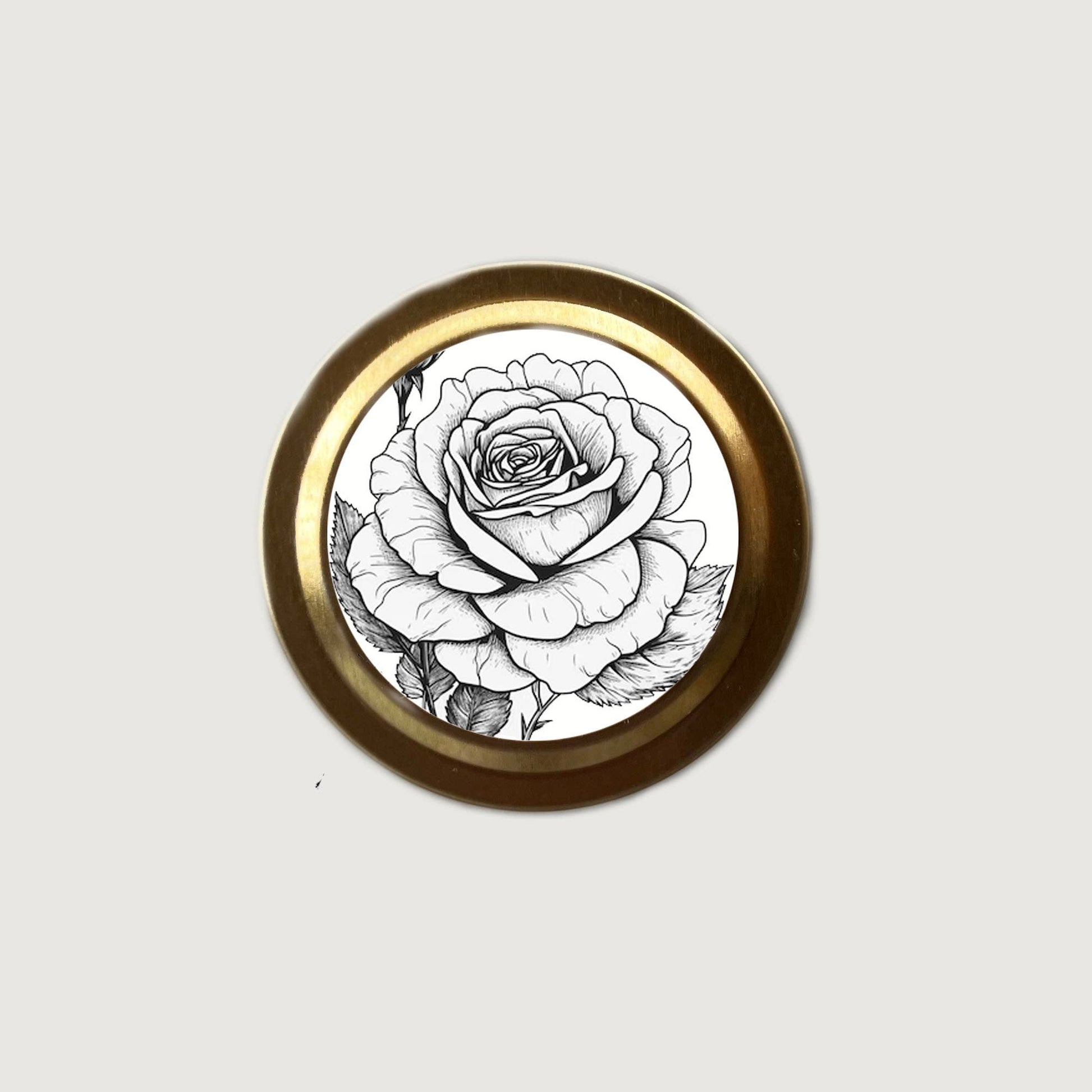 Round decorative item with a black and white rose design on a gold rim against a light gray background