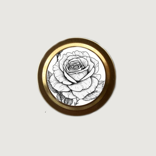 Round decorative item with a black and white rose design on a gold rim against a light gray background