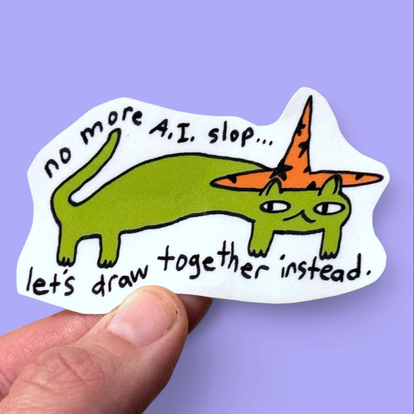 A hand holding a die-cut sticker featuring a green cartoon cat wearing an orange pointed hat, with handwritten text that reads 'no more A.I.