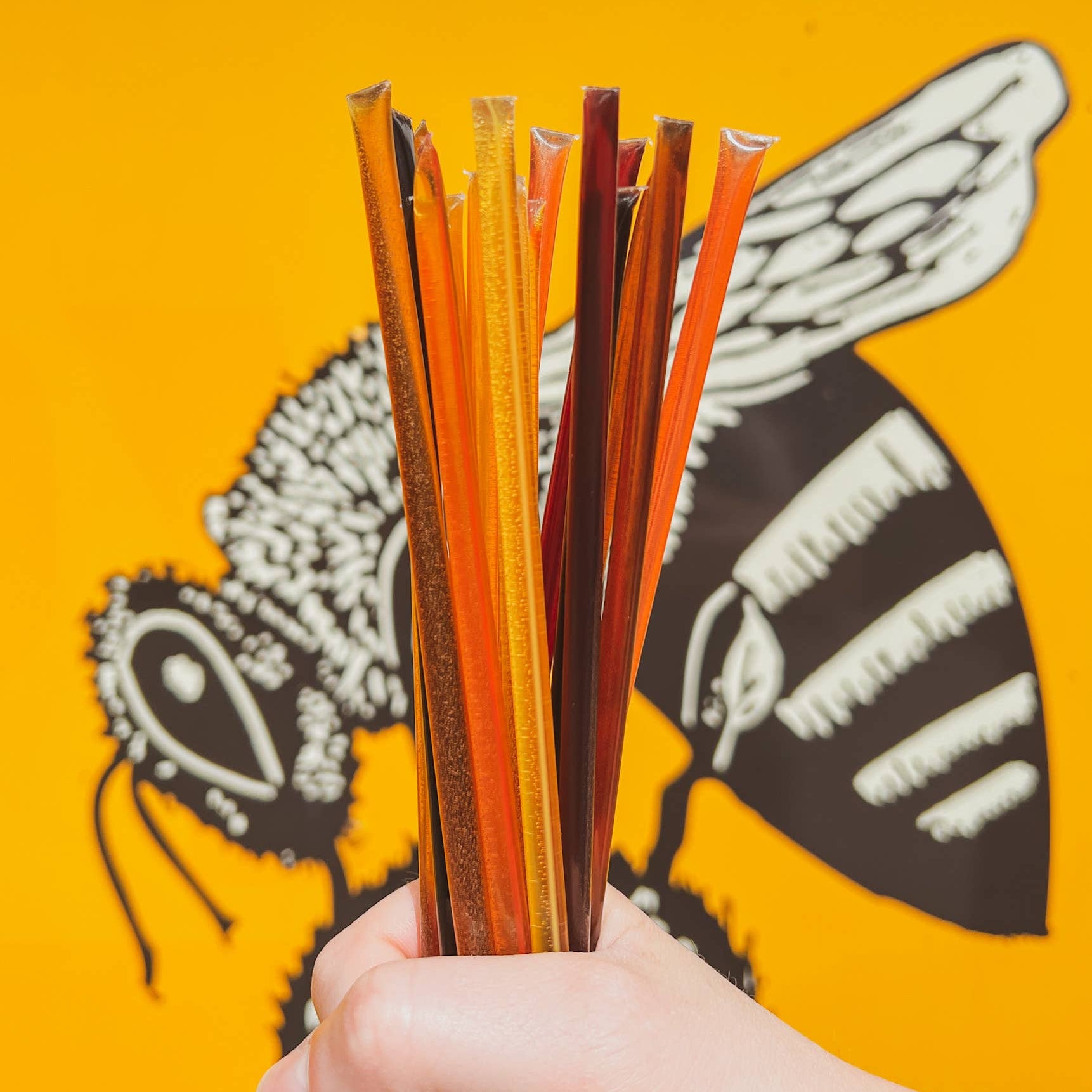 Hand holding colorful straws against a yellow background with butterfly design