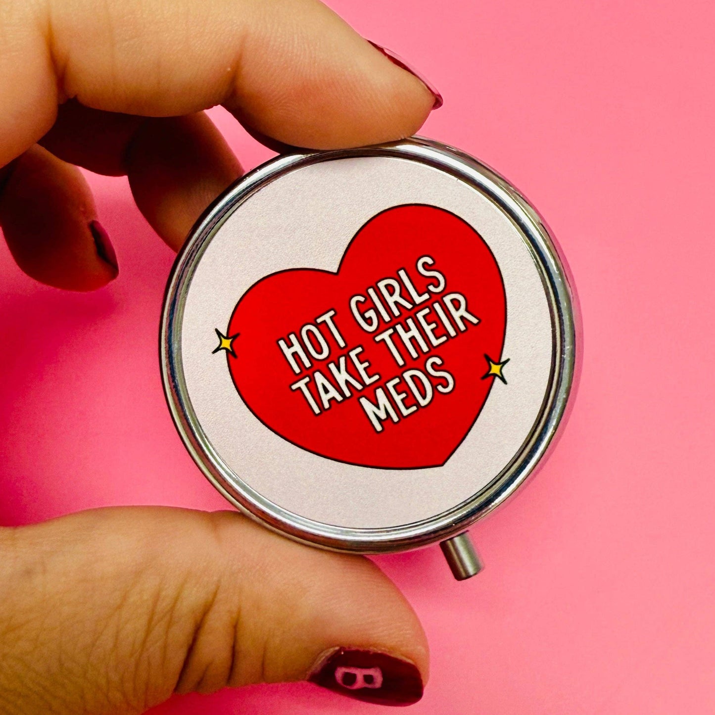 Hand holding a pill case with a red heart and text on a pink background