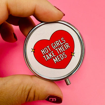 Hand holding a pill case with a red heart and text on a pink background