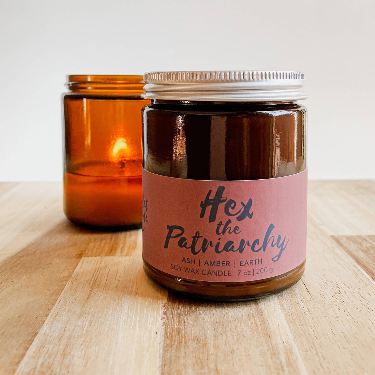 Candle jar with a pink label reading 'Hex the Patriarchy' on a wooden surface.