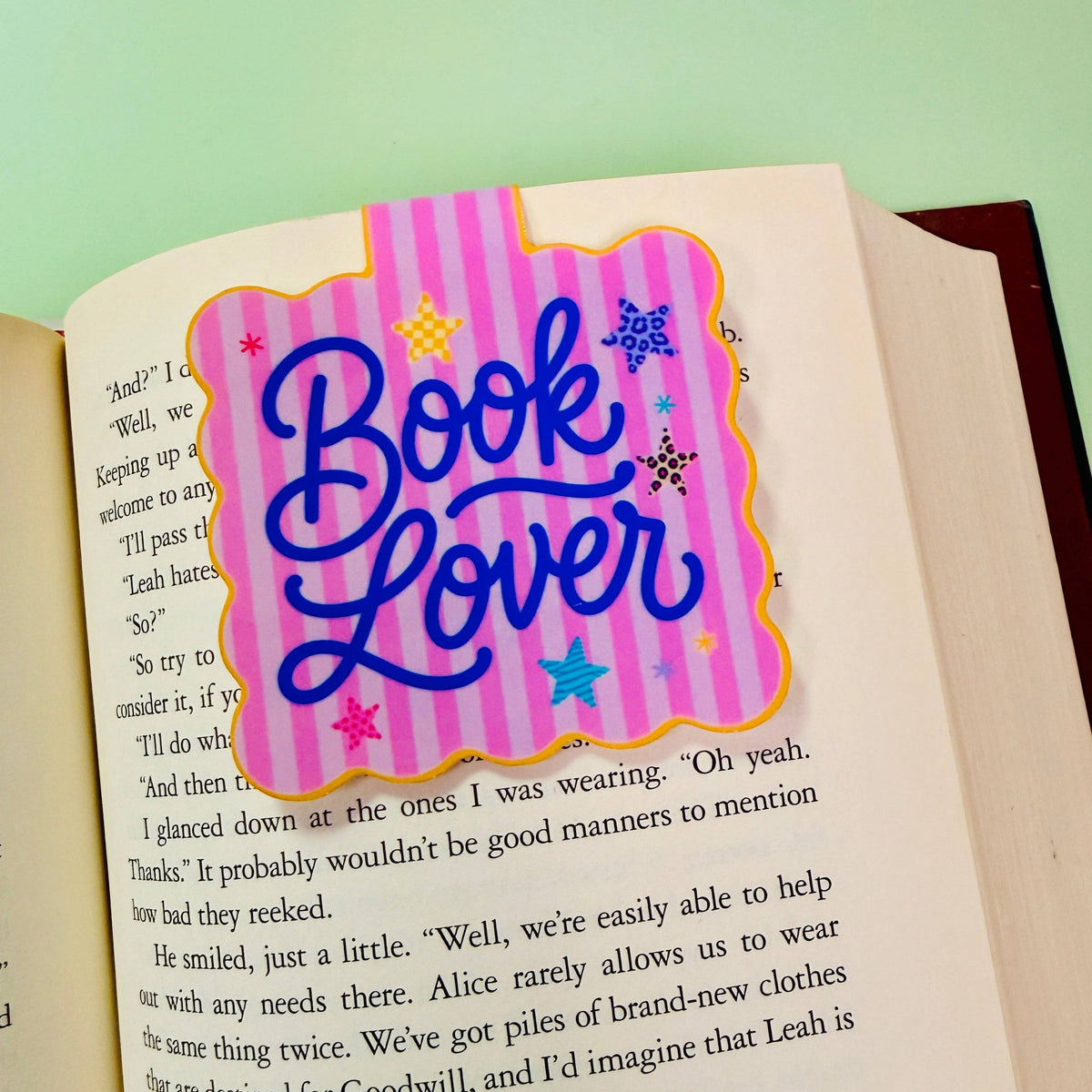 A decorative book lover bookmark with the words 'Book Lover' in blue script on a pink striped background, placed on an open book page.