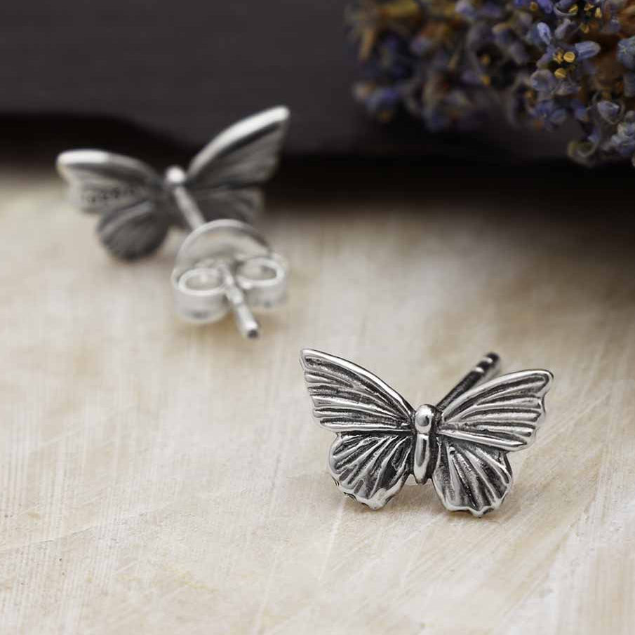 Butterfly-shaped silver earrings on a textured surface with dried lavender flowers.