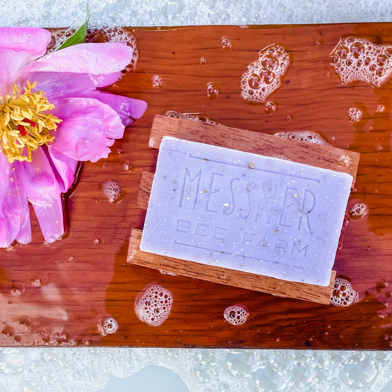 Bar of soap with 'Messed Up' branding on a wooden board with bubbles and a pink flower.