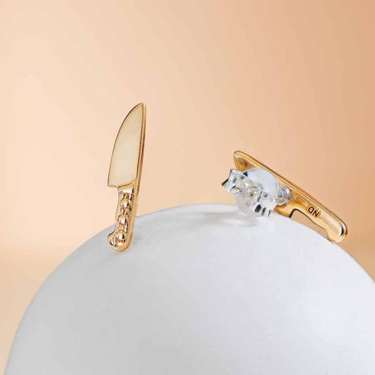Gold and silver earrings on a white sphere with a beige background