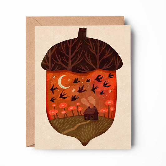 A square greeting card with a kraft envelope behind it, featuring an illustrated acorn design. The acorn cap is dark brown with bare tree branches, while the interior shows a warm orange and red landscape with a crescent moon, flying birds, small flowers, and a tiny house on a beige card background.