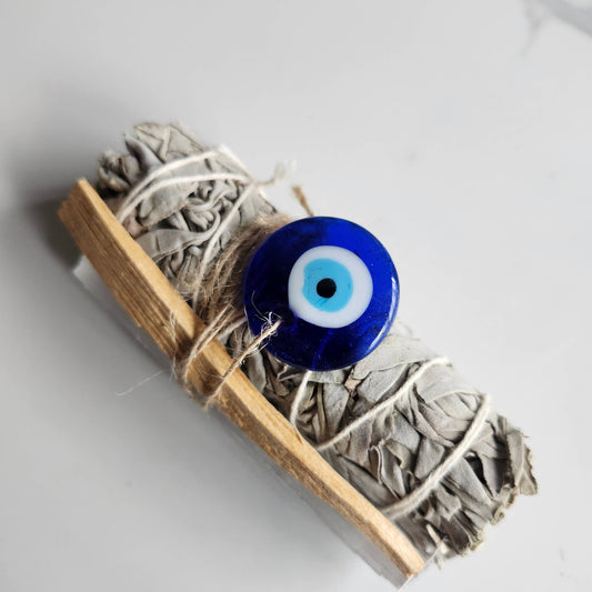 Incense stick wrapped with twine and featuring a blue evil eye charm on a light gray background