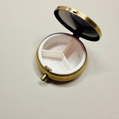 Round brass pill box with white interior on a light gray background