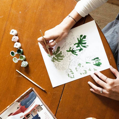 Person painting on paper with a cup of coffee and art supplies on a wooden table
