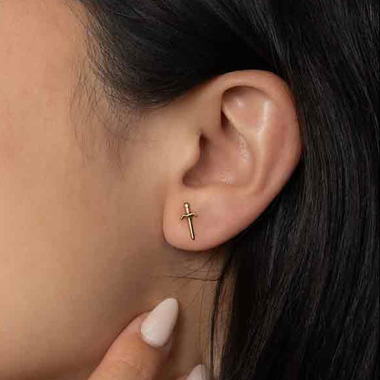 Close-up of a woman wearing a gold cross earring with a neutral background