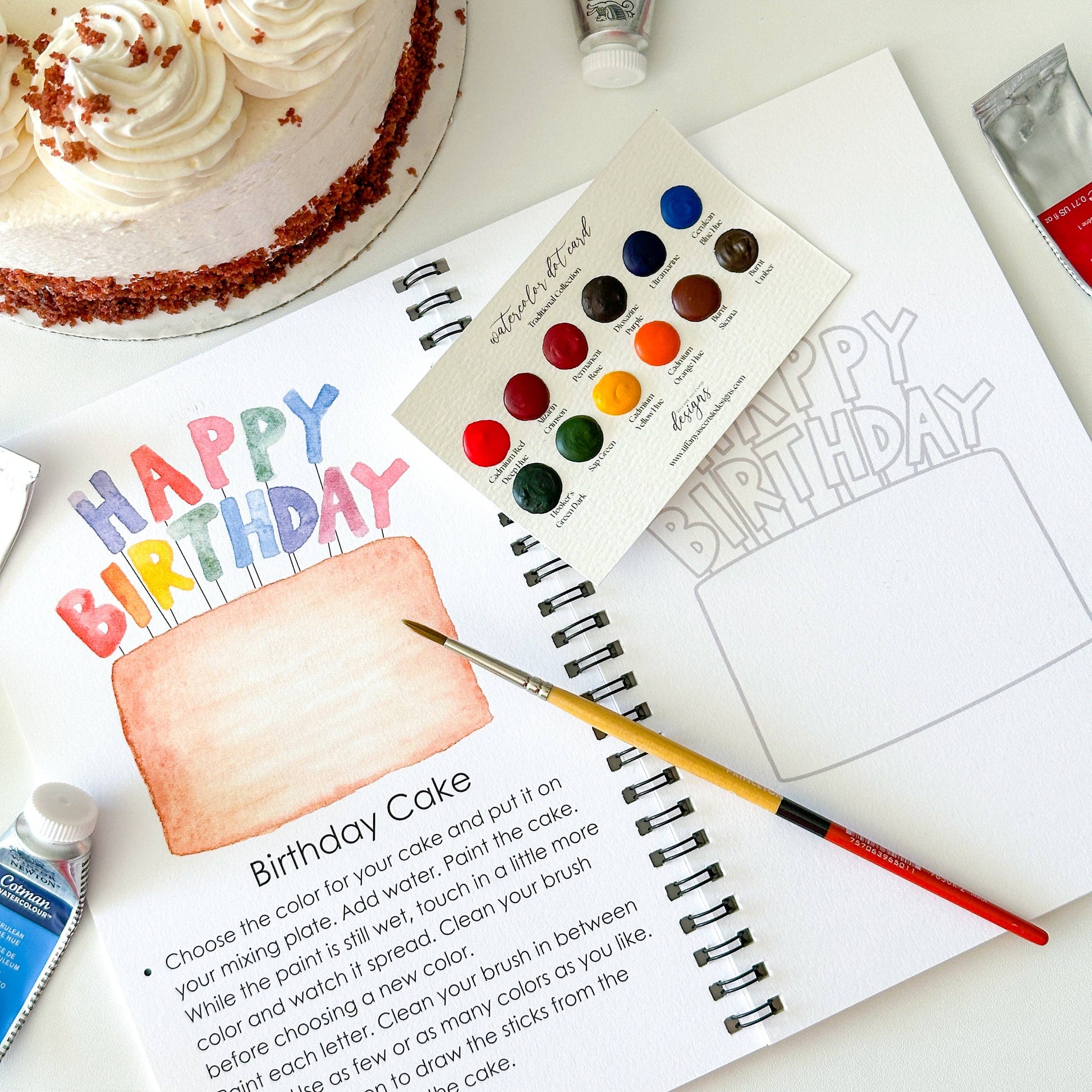 Artistic birthday cake coloring book with watercolor paints and a cake on a table.