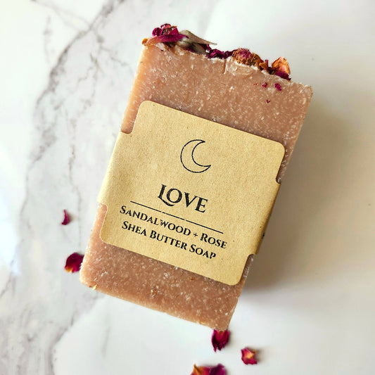 Bar of sandalwood and rose shea butter soap with a 'LOVE' label on a marble surface.
