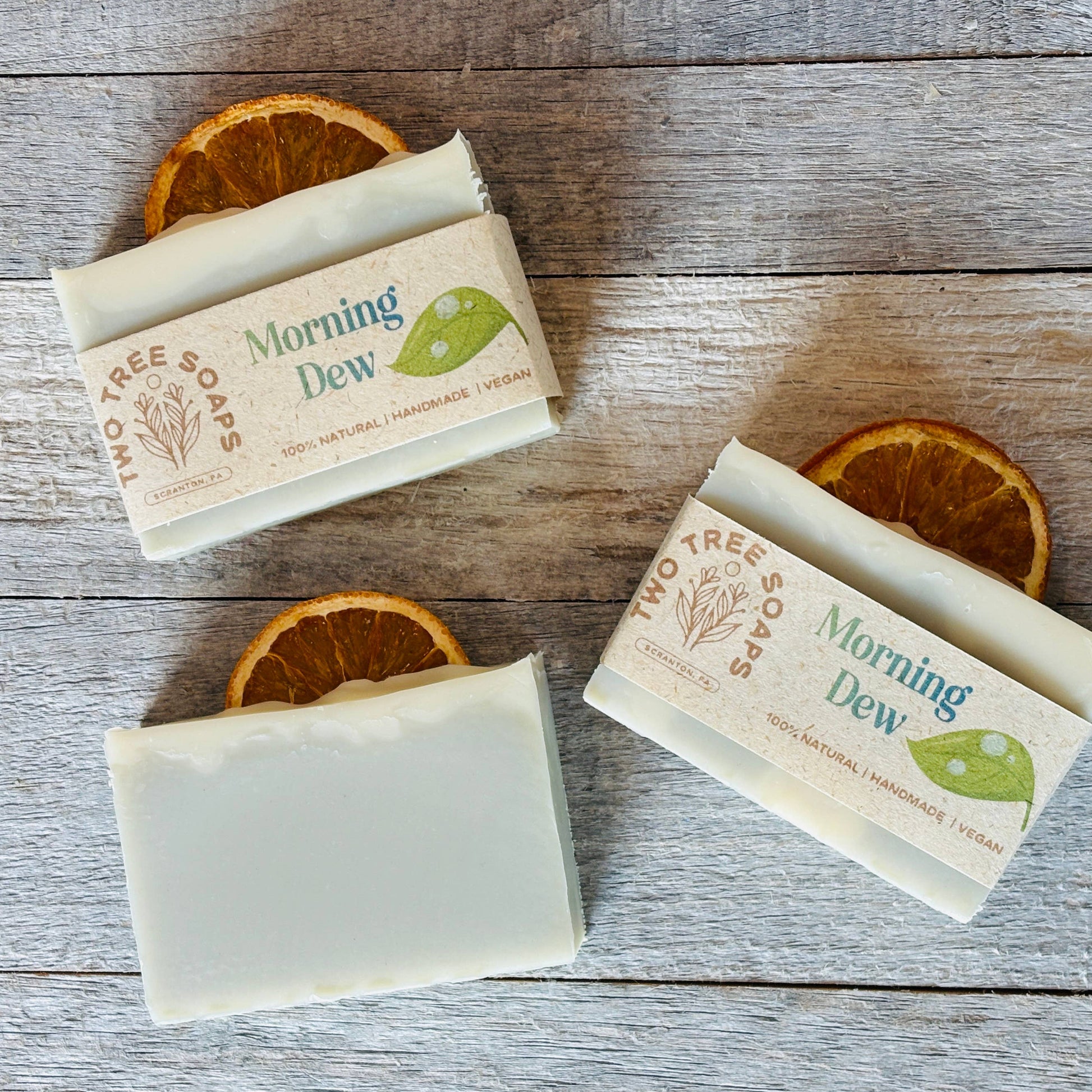 Three bars of 'Morning Dew' soap on a wooden surface with orange slices.