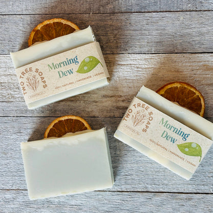 Three bars of 'Morning Dew' soap on a wooden surface with orange slices.
