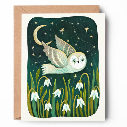 A square greeting card with a kraft envelope, featuring an illustration of a white owl flying at night under a crescent moon and stars, with snowdrop flowers at the bottom.