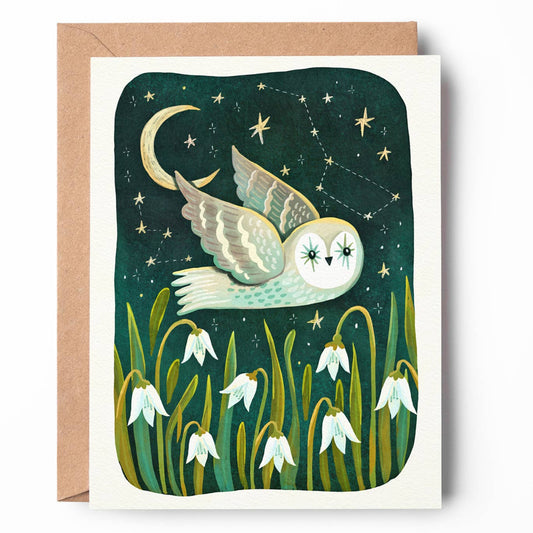 A square greeting card with a kraft envelope, featuring an illustration of a white owl flying at night under a crescent moon and stars, with snowdrop flowers at the bottom.