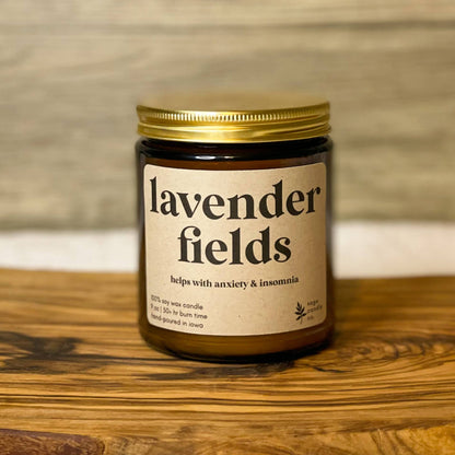 A candle jar labeled 'lavender fields' sits on a rustic wooden board against a light wood wall and white fabric background.