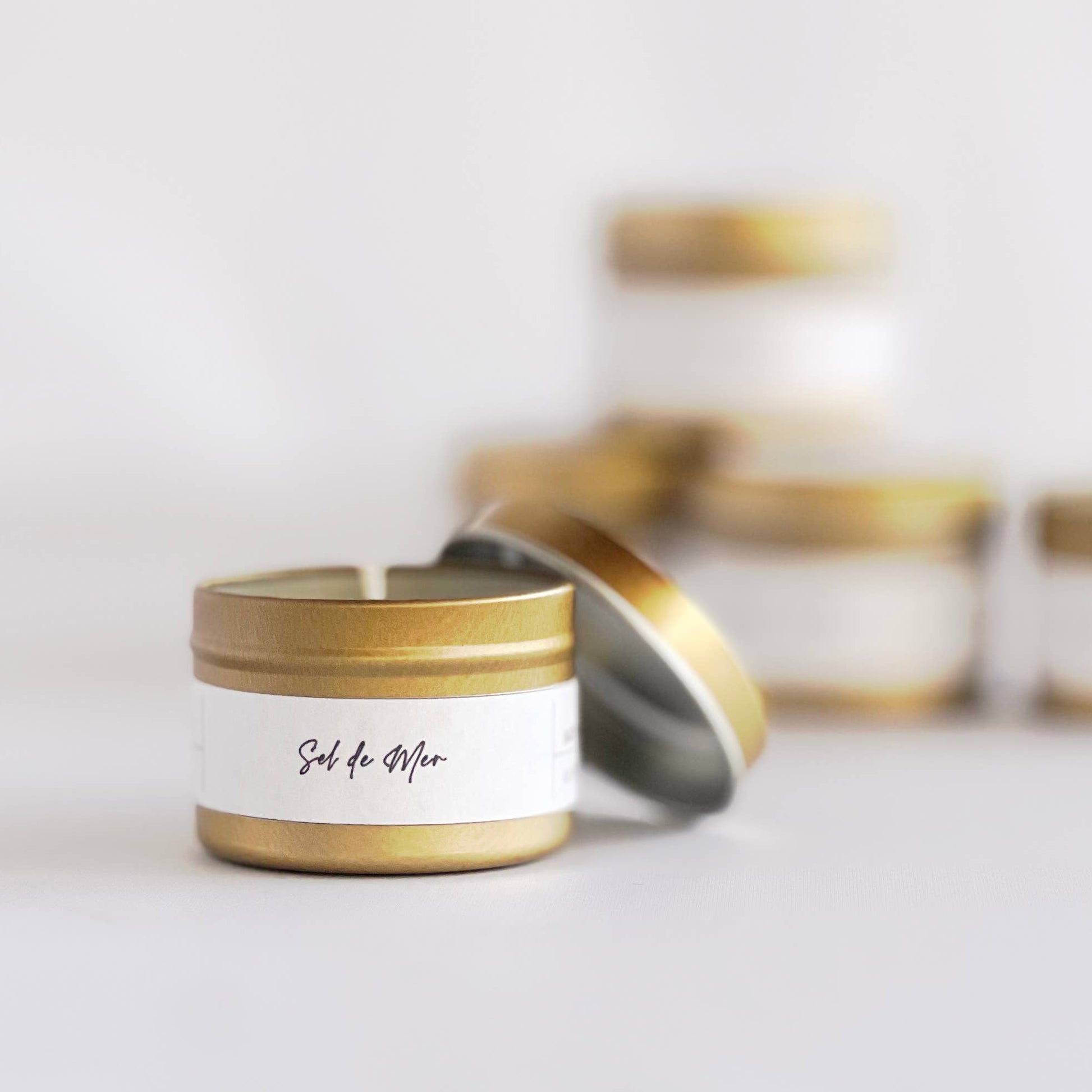 Candle in a gold jar with a white label on a light gray background
