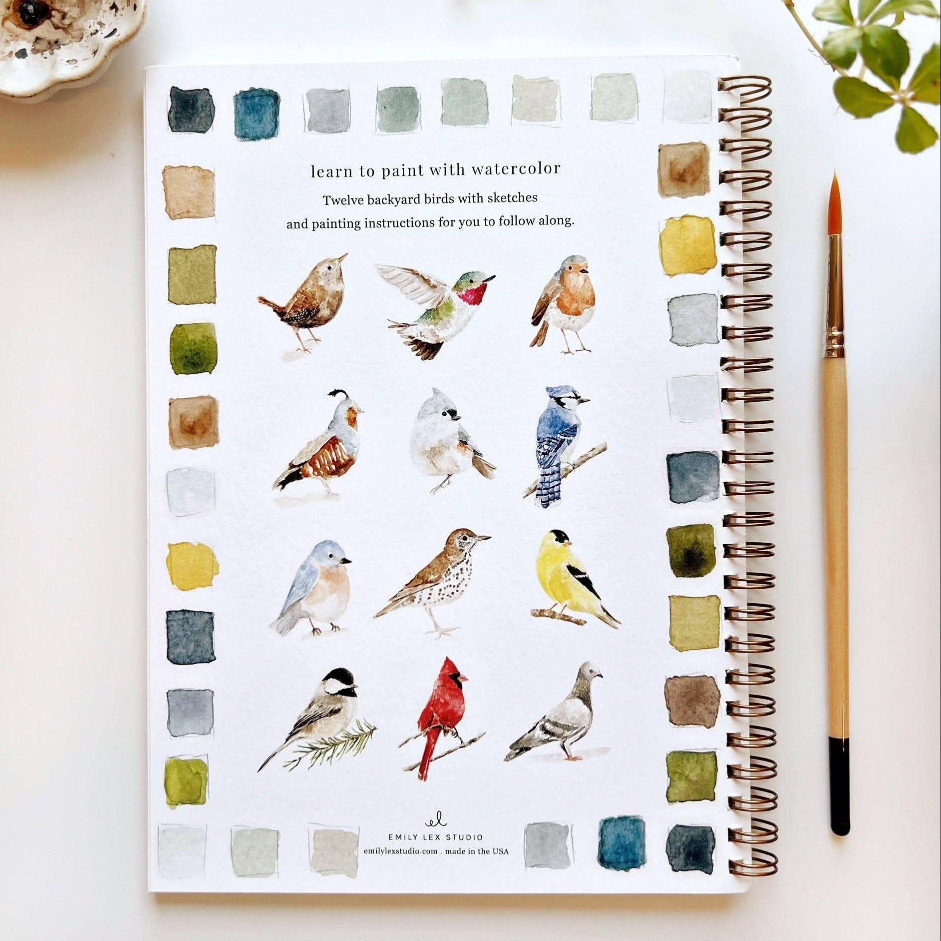 Notebook with watercolor illustrations of birds and a paintbrush on a white surface