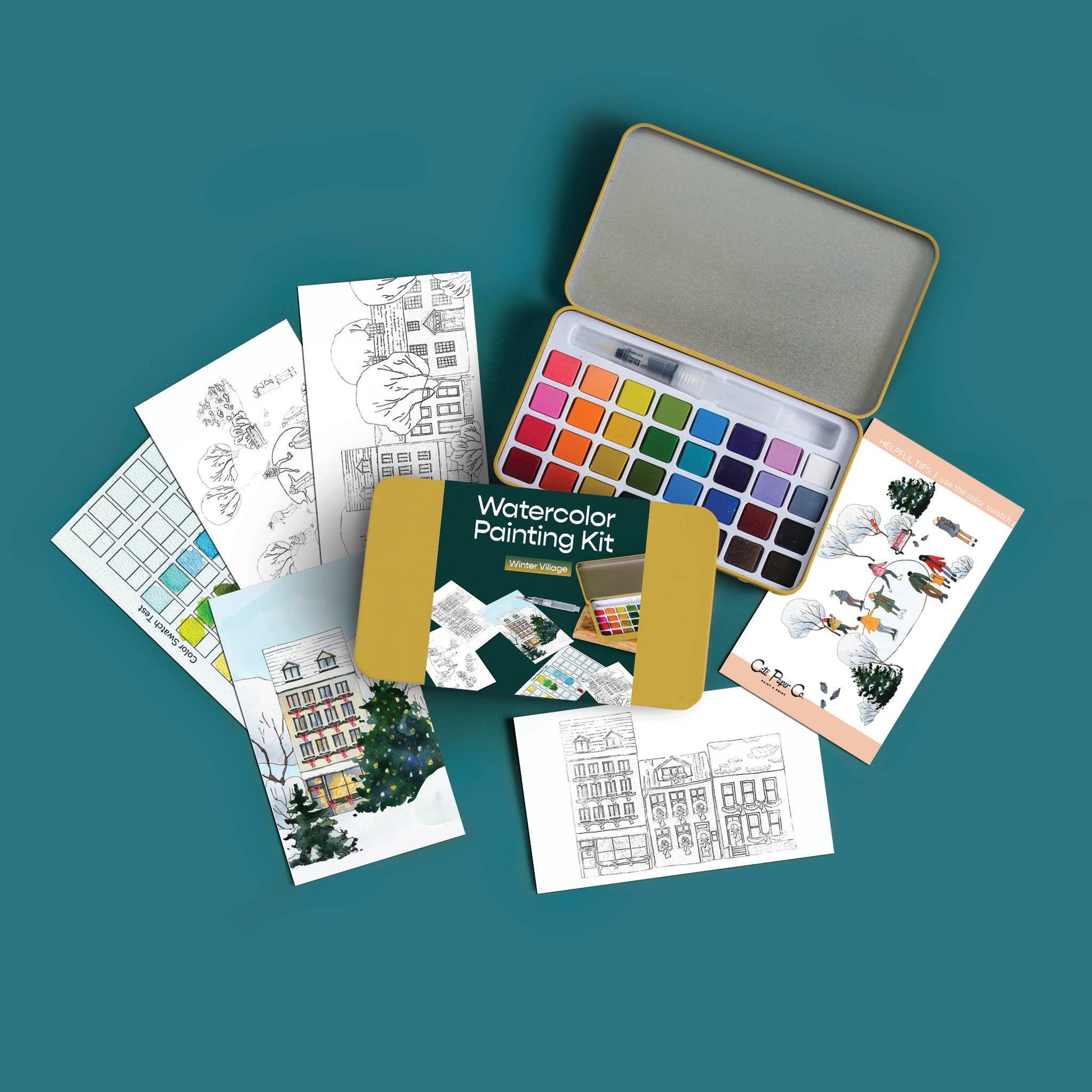 An open watercolor painting kit with a metal palette of many colors, surrounded by printed art cards and sketch sheets on a teal background.