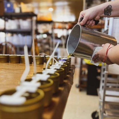 Person pouring liquid into small containers on a wooden shelf.|418