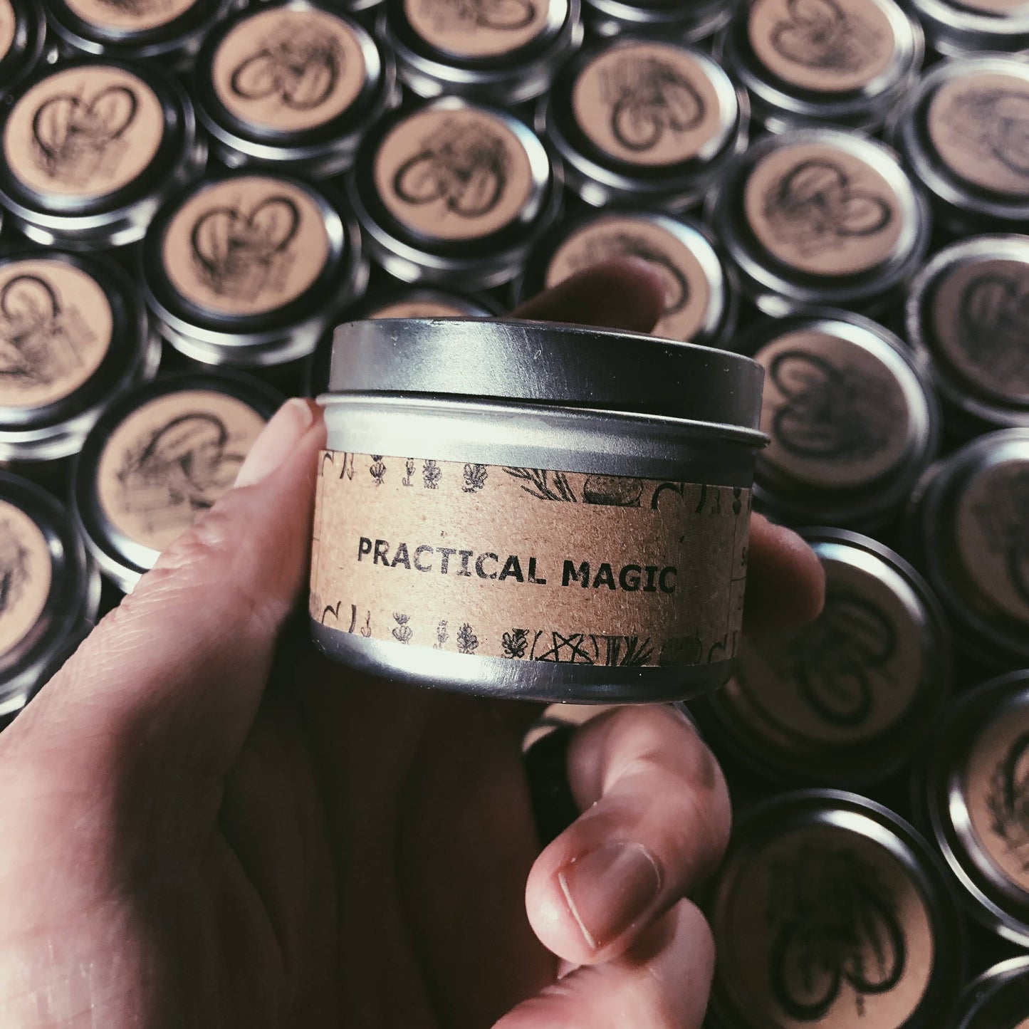 Hand holding a small container labeled 'Practical Magic' against a background of similar containers.