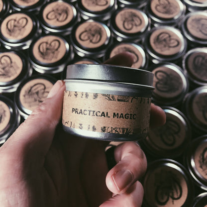 Hand holding a small container labeled 'Practical Magic' against a background of similar containers.
