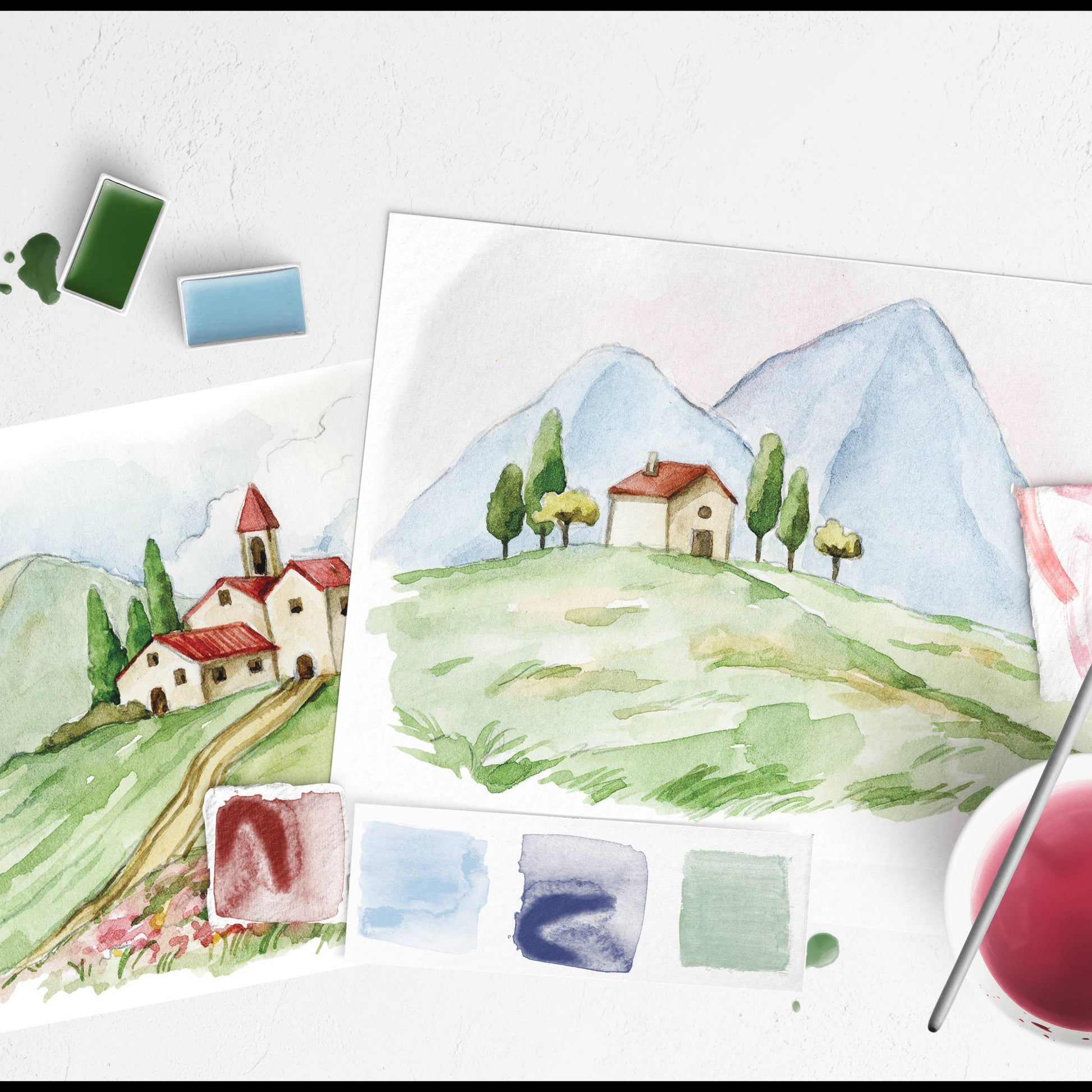 Watercolor landscape painting with mountains and houses, surrounded by paint swatches and a brush.