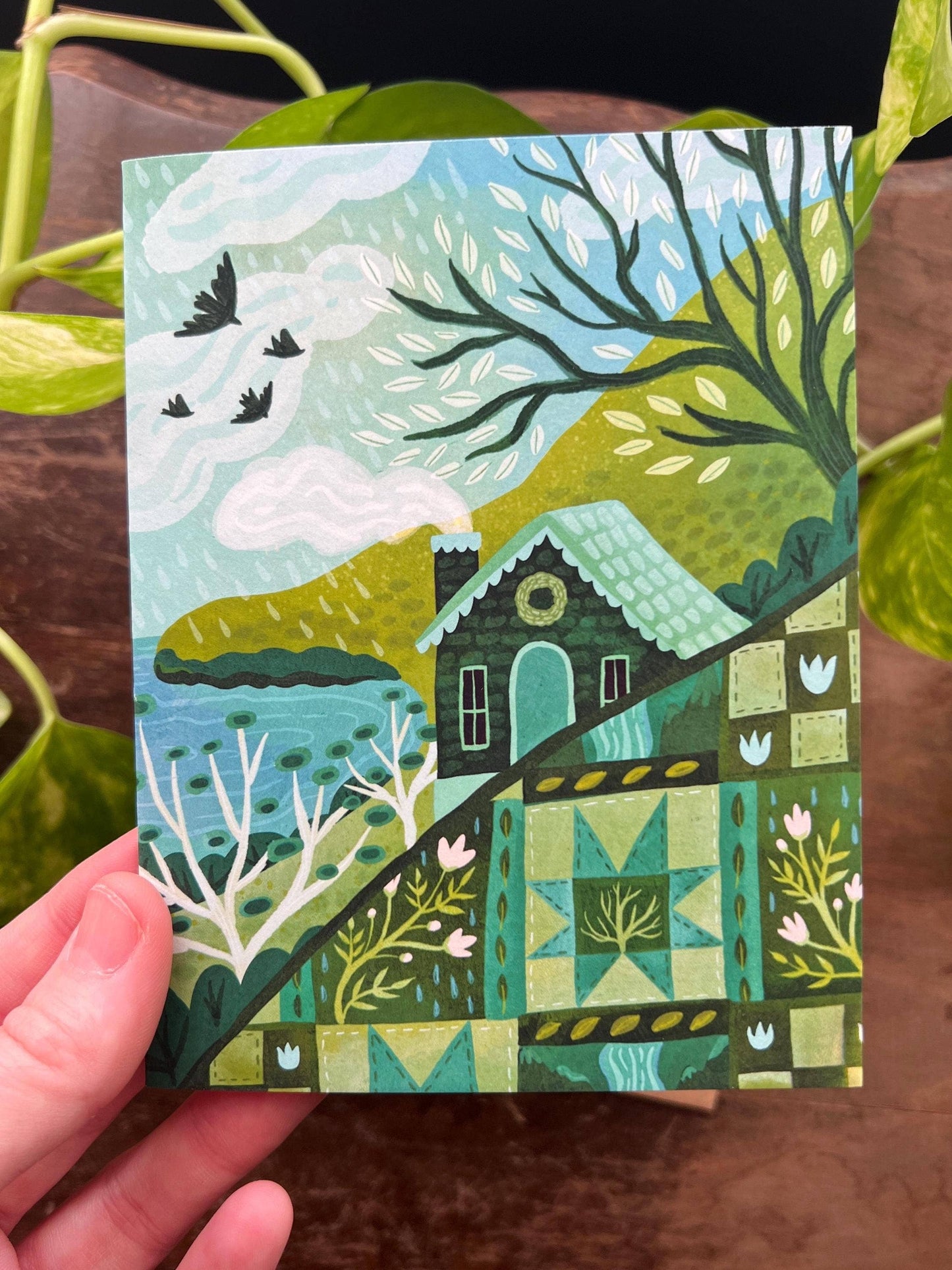 Hand holding a colorful card with a house and nature design.