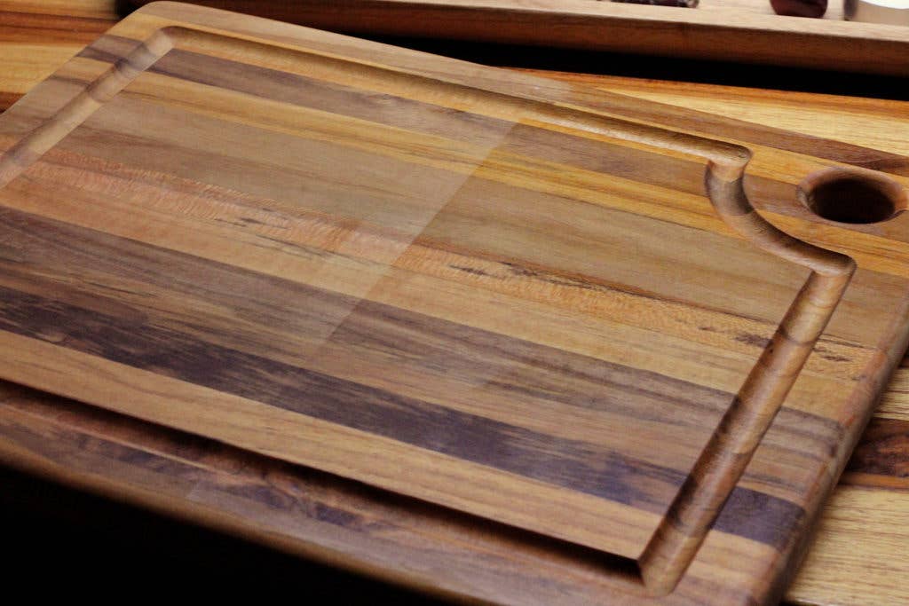 A rectangular wooden cutting board with a rounded handle cutout, featuring a striped natural wood grain pattern in shades of brown and tan.