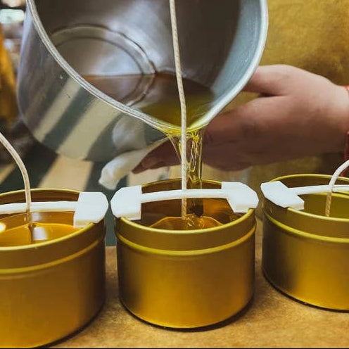 Person pouring liquid into small metal containers on a wooden surface.